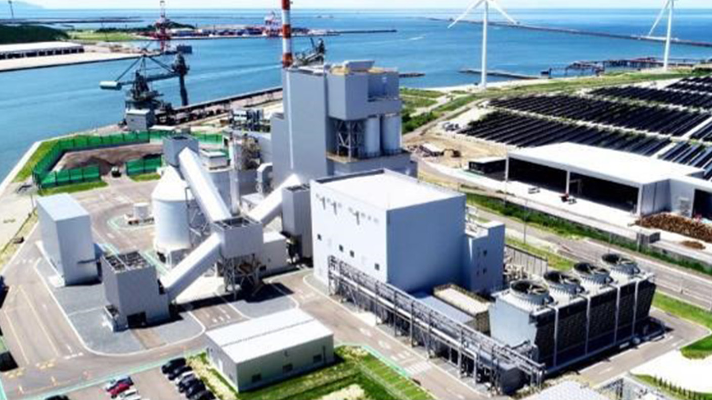 An electricity station with wind turbines and sea in the background